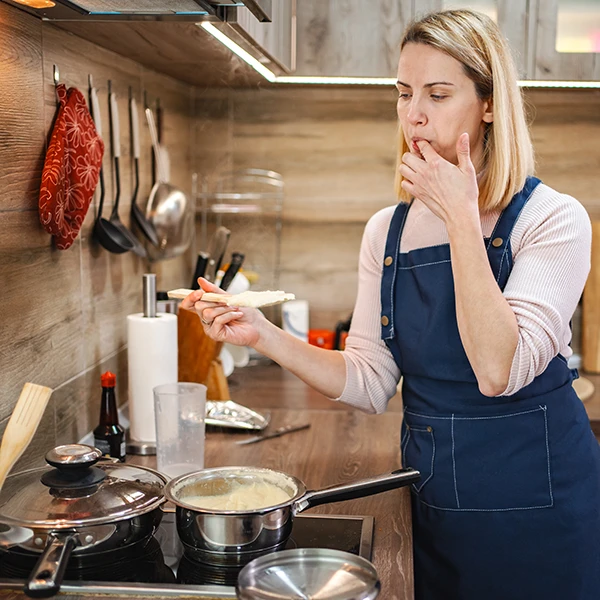 Naine köögis maitsestab toitu, pliidil mitu potti ja panni korraga